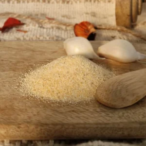 Ail semoule posé sur une planche en bois avec une cuillère en bois et des gousses d'ail entières en fond d'image