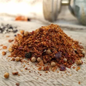 Un mélange de piment en flocons, de coriandre et poivre noir concassé. Ceci posé sur une planche en bois avec un globe en fond.