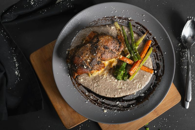 Une assiette noire avec un morceaux de viande et quelques légumes accompagnés d'une sauce au poivre