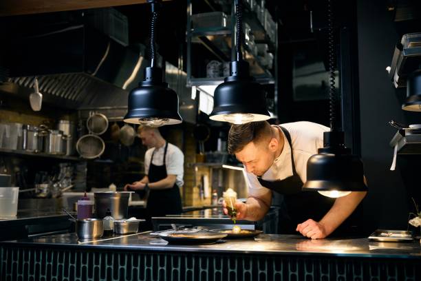 Un chef de cuisine qui dresse une assiette en ajoutant une vinaigrette sur sa préparation.