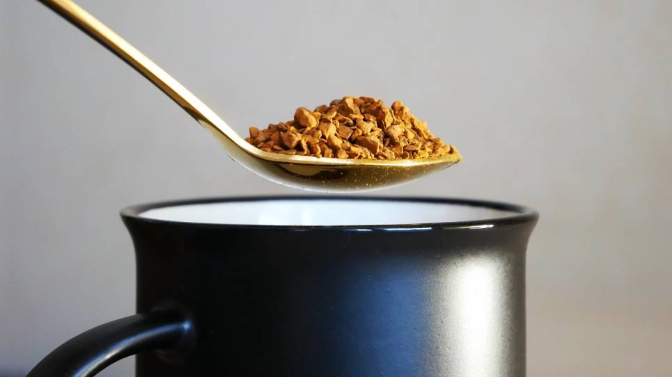 Une cuillère de café prêt à être versée dans une tasse à café