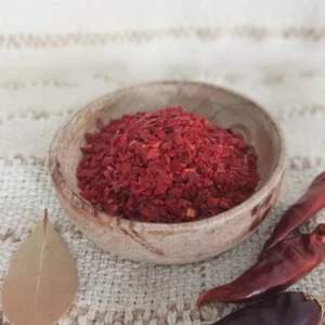 Piment Gochugaru vu éloignée dans une coupelle en bois avec des piments entiers à droite et une feuille de laurier à gauche